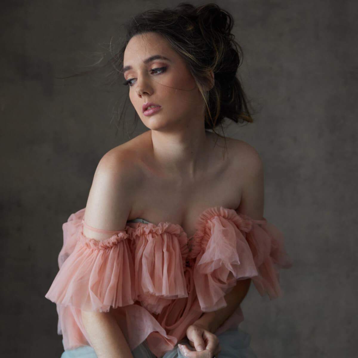 Before: Portrait of a woman in a pink ruffled off-the-shoulder top against a grey wall