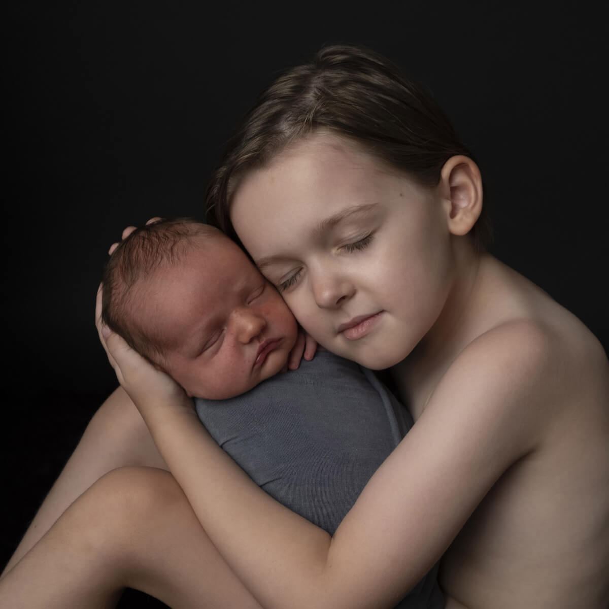 Before: Boy holding a sleeping newborn against a black background