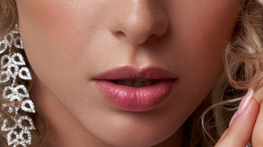 Close-up of a woman’s lips and chin with curly blonde hair and ornate earrings
